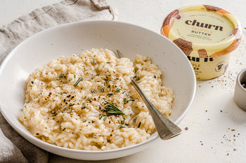 Creamy truffle risotto with rosemary and black pepper in a white bowl, beside a container of Churn Truffle Butter.