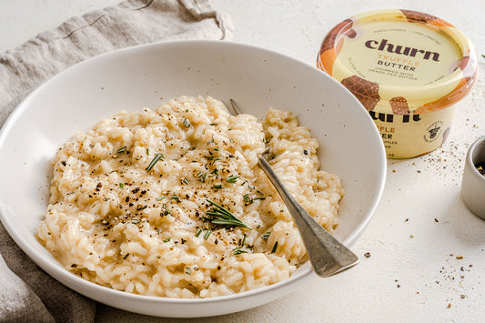 Creamy truffle risotto with rosemary and black pepper in a white bowl, beside a container of Churn Truffle Butter.