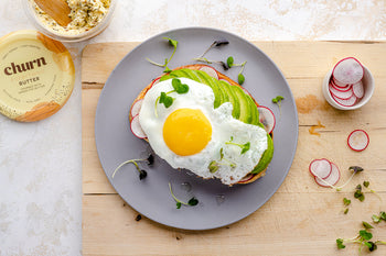 Avocado toast topped with a sunny-side-up egg, avocado slices, radishes, and microgreens, paired with Churn Everything Butter.