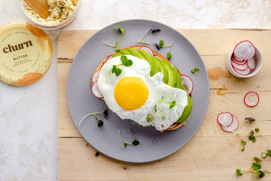 Avocado toast topped with a sunny-side-up egg, avocado slices, radishes, and microgreens, paired with Churn Everything Butter.