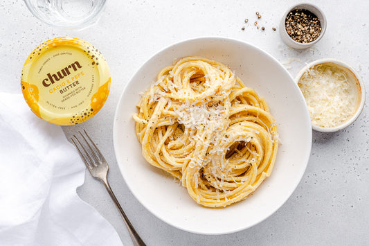 Bowl of creamy Cacio e Pepe pasta topped with cheese and pepper, served with Churn Cacio e Pepe Butter, fork, and grated cheese.