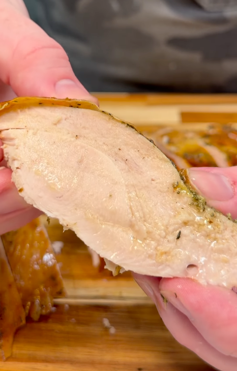 Hands holding a thick slice of juicy herb-roasted turkey breast showing a moist, tender interior.
