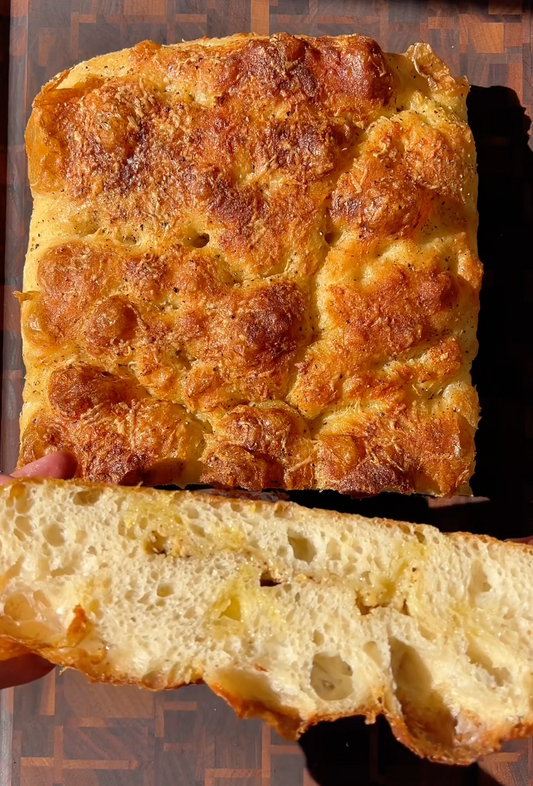 Golden-brown focaccia topped with melted cheese, shown whole and sliced to reveal a light, airy crumb.