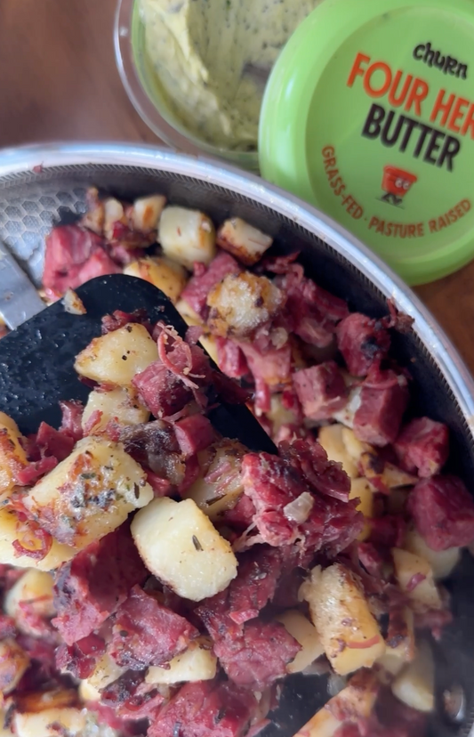 Skillet hash with crispy potatoes and corned beef, served with herb butter in the background.